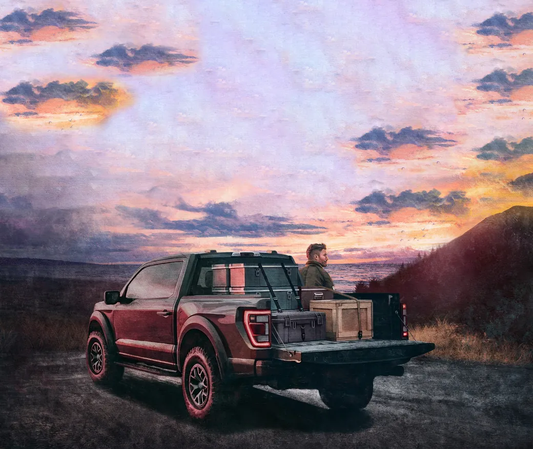 Concept art: a driver sitting on the tailgate of a loaded pickup, watching a coastal sunset.